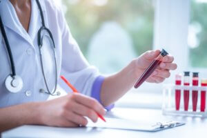 Professional general medical doctor examines blood sample from a vein and writes the results to the clipboard in hospital